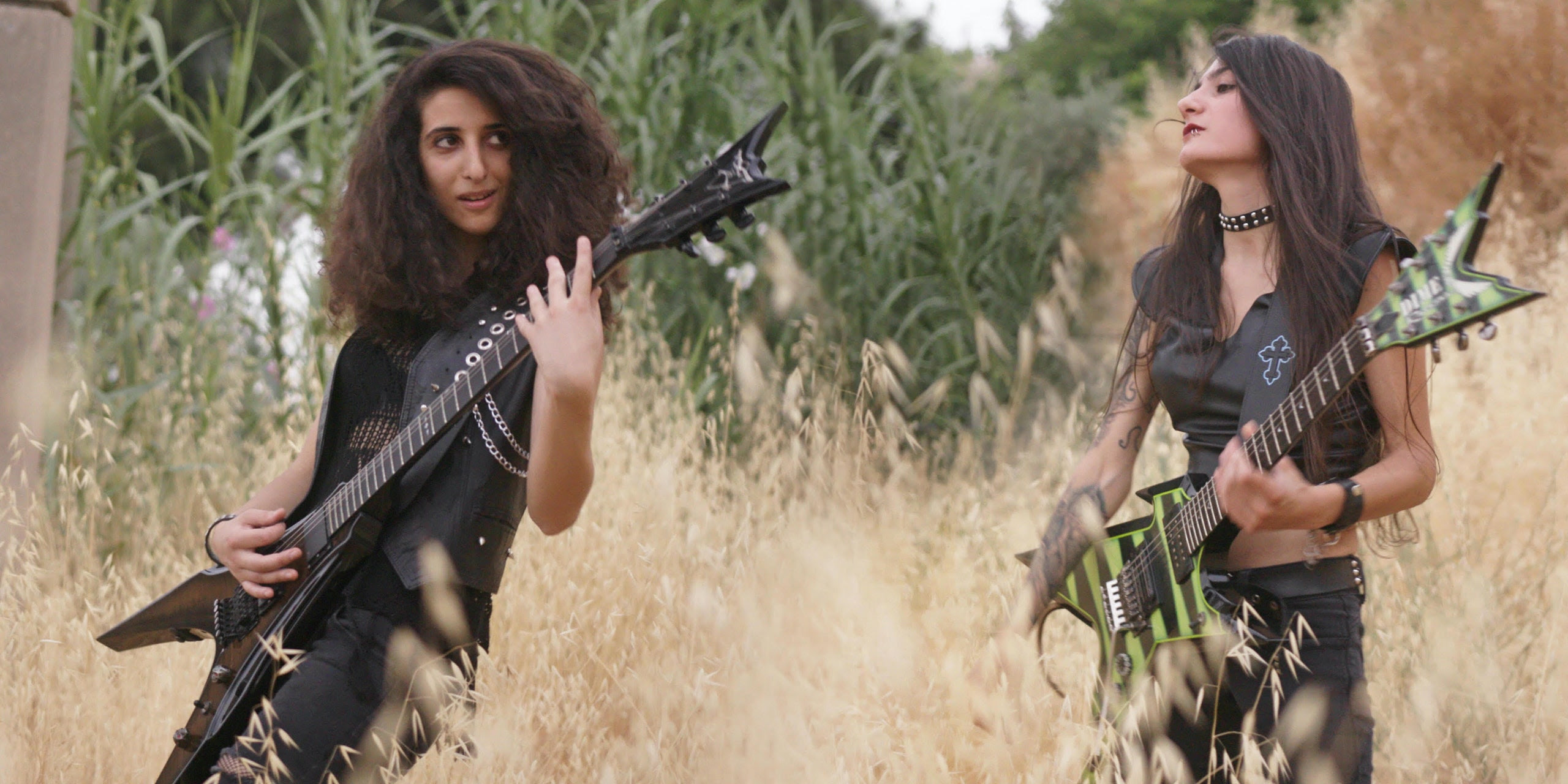 Two women, both with long brown hair and wearing sleeveless vests, perform on their electric guitars in a field of uncut wheat and grass. From Rita Baghdadi's 'Sirens," which is showing in theaters through Oscilloscope Laboratories. Courtesy of Oscilloscope Laboratories . 