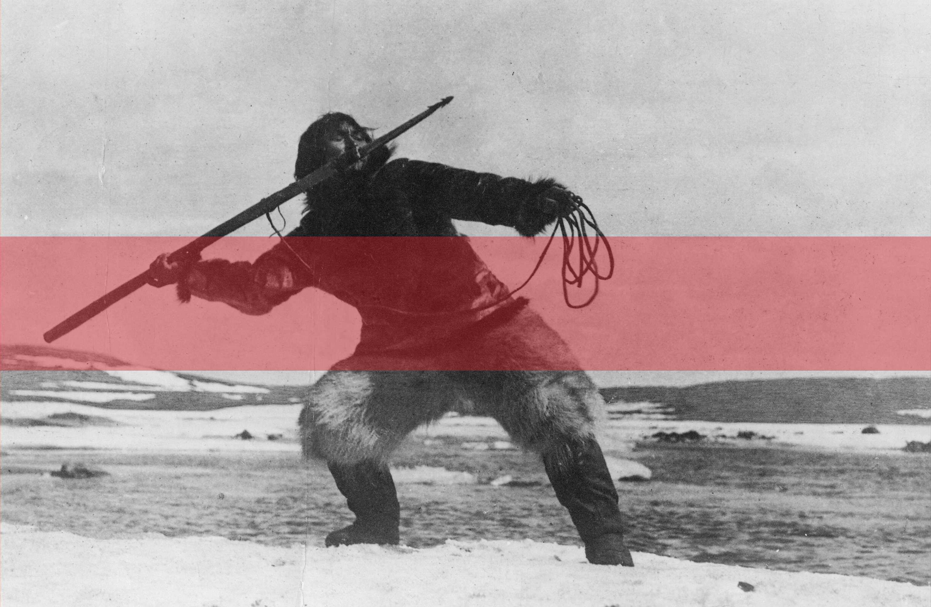A man standing on an icy landscape wields a harpoon towards the water. From Robert Flaherty's ‘Nanook of the North.’