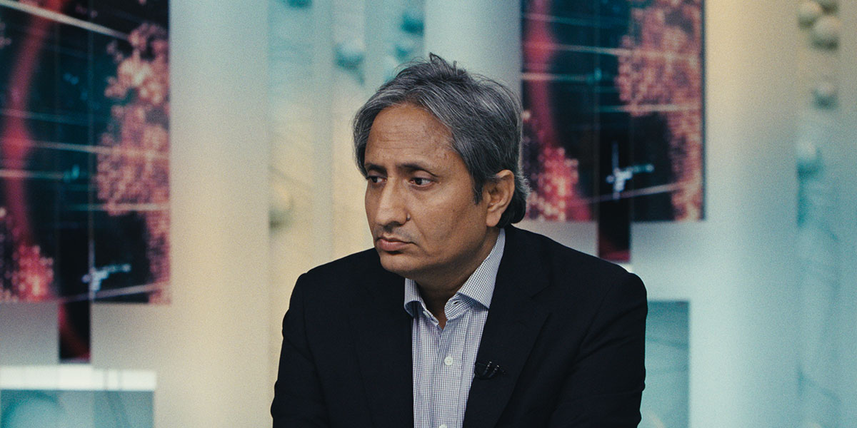 Indian TV journalist Ravish Kumar has gray hair, a black blazer and a white shirt. He sits pensively in a TV news room. From Vinay Shukla’s ‘While We Watched.’ Courtesy of IDFA
